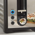 Black and silver toaster with illuminated reheat and defrost buttons, close-up