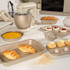Gold non-stick bakeware set with croissants, tarts, and stand mixer on kitchen worktop