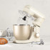 Cream stand mixer with metal bowl on kitchen counter, surrounded by baking pastries.