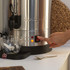 Hand dispensing hot water into a glass cup from a silver catering urn