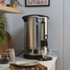 Hand pouring water into stainless steel hot water urn on kitchen counter