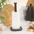 Black kitchen roll holder with roll, shown on worktop beside black kettle