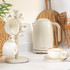 Cream ceramic mugs and kettle on a kitchen counter, with wooden utensils in background