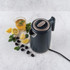 Dark grey electric kettle with a cup of mint tea, lemons, blackberries, and mint on table