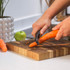 Hands peeling a carrot with a black peeler on a wooden chopping board in a kitchen