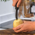 Black-handled peeler removing eyes from a potato on wooden chopping board