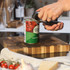 Hand using can opener to open tin of chopped tomatoes on wooden chopping board