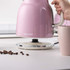 Pink electric kettle on base, hand holding handle, next to pink mug on kitchen worktop