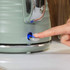 Sage green electric kettle being switched on, showing blue power light.