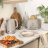 Taupe cordless electric kettle pouring hot water into grey mug, shown in use