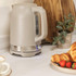Taupe electric kettle on kitchen counter next to plate with croissants and strawberries.