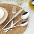 Stainless steel cutlery set with fork, knife, dessert spoon and teaspoon on woven placemat