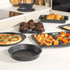 Set of black speckled non-stick baking trays and cake tin with cooked food, on kitchen counter