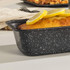 Black speckled loaf tin with baked lemon cake, sliced lemons on top