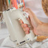 Cream hand mixer with chrome accents, shown in use, kitchen setting