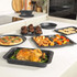 Set of grey speckled non-stick oven trays and tins shown with cooked food in modern kitchen