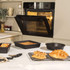 Non-stick black bakeware on kitchen counter with oven, including tin and cooling rack.