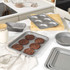 Set of grey non-stick metal bakeware shown on kitchen counter, with cookies and baking accessories.