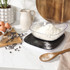 Black digital kitchen scale with assorted nuts on top, next to a bowl of mixed nuts