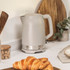 Taupe electric kettle on kitchen countertop, shown with wooden utensils and croissant.