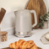 Taupe electric kettle on kitchen countertop, shown with wooden utensils and croissant.