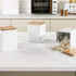 Set of three white kitchen storage containers with wood lids, one open showing tea bags.