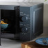 Grey microwave oven with mechanical dials shown heating food, door open