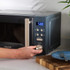 Grey microwave oven on kitchen counter, person setting timer with hand, plate and fork beside.