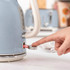 Blue electric kettle with cream handle, power switch being pressed on a kitchen counter.