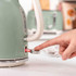 Finger pressing switch on green electric kettle, close-up for product feature.