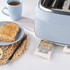 Blue 4-slice toaster with crumb tray extended, next to plate with toast and mug.