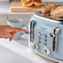 Light blue four-slice toaster with seeded bread, being operated by hand, on kitchen counter