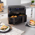 Black dual drawer air fryer on kitchen counter, drawers open, with plates of food beside.