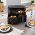 Black dual drawer air fryer on kitchen counter with cooked chips and vegetables