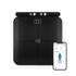 Black smart bathroom scale with digital display and smartphone app showing body analysis.