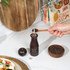 Acacia wood pepper grinder on kitchen counter, next to black pepper and salad.