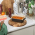 Loaf tin with baked orange-topped cake on wooden board, shown in a kitchen setting