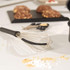 Stainless steel whisk with black handle on kitchen worktop, baking ingredients in background