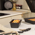 Black non-stick loaf tin with baked loaf topped with dried citrus slices, kitchen setting