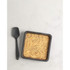 Square black tin filled with golden crumble topping beside a black spatula, shown overhead.