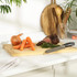 Kitchen scene with wooden chopping board, chef knife, carrots, onion and sliced beef joint.