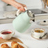 Light green stovetop kettle pouring hot water into teacup in kitchen setting
