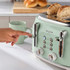 Mint green 4-slice toaster with bagels toasting, hand pressing lever