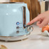 Hand pressing lever on light blue 2-slice toaster with cancel, reheat and defrost buttons