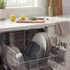 Open dishwasher with clean grey plates, glassware and cutlery in kitchen setting