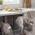 Open dishwasher filled with clean plates, glasses and cutlery in modern kitchen