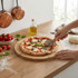 Person cutting margherita pizza with pizza cutter on wooden board in kitchen