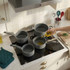 Set of four grey saucepans on induction hob, oil being poured into one pan