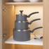 Stacked set of three grey non-stick saucepans with lids and handles in a kitchen cupboard