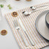 Set of silver hammered cutlery on striped napkin beside plate and dried citrus slice